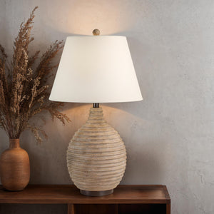 Cebada table lamp by Renwil on a wooden table next to a vase, with a textured wall in the background.