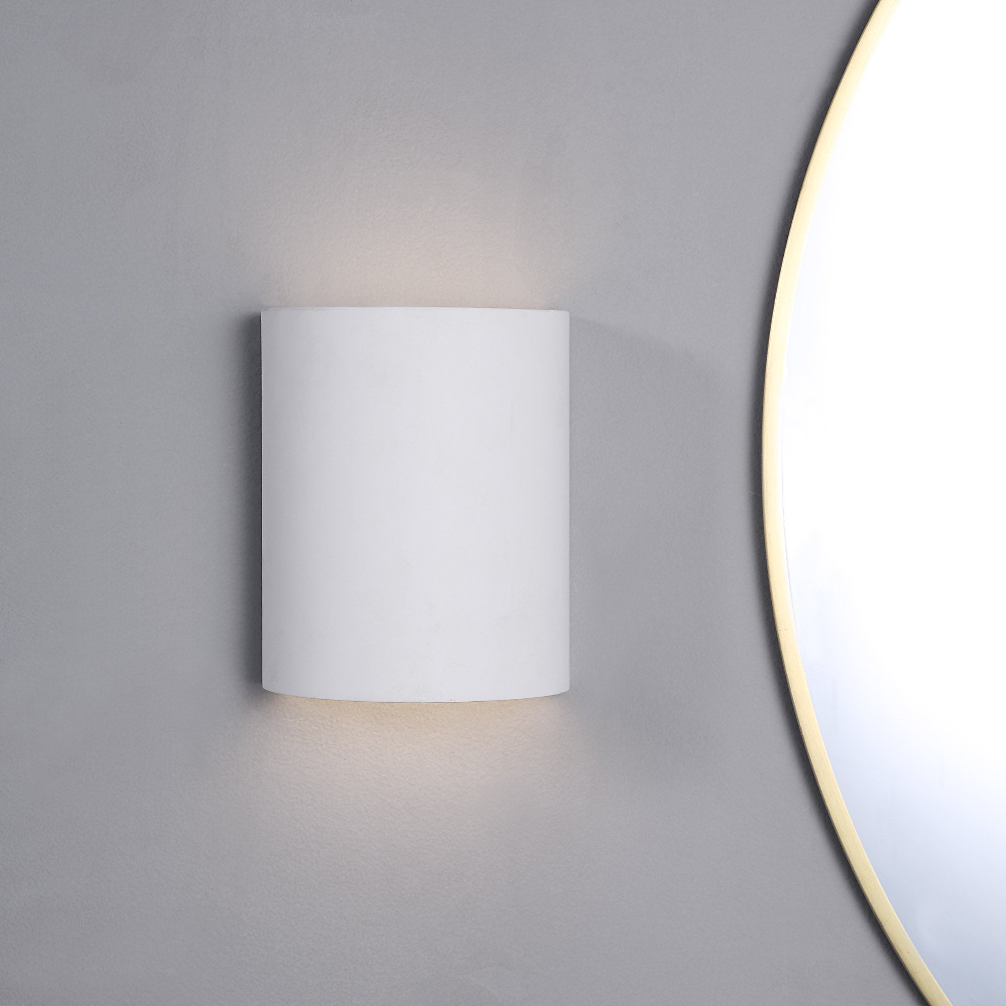 Ladee Wall Sconce in white mounted on a gray wall, illuminating softly.