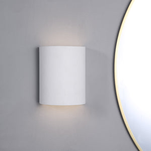 Ladee Wall Sconce in white mounted on a gray wall, illuminating softly.
