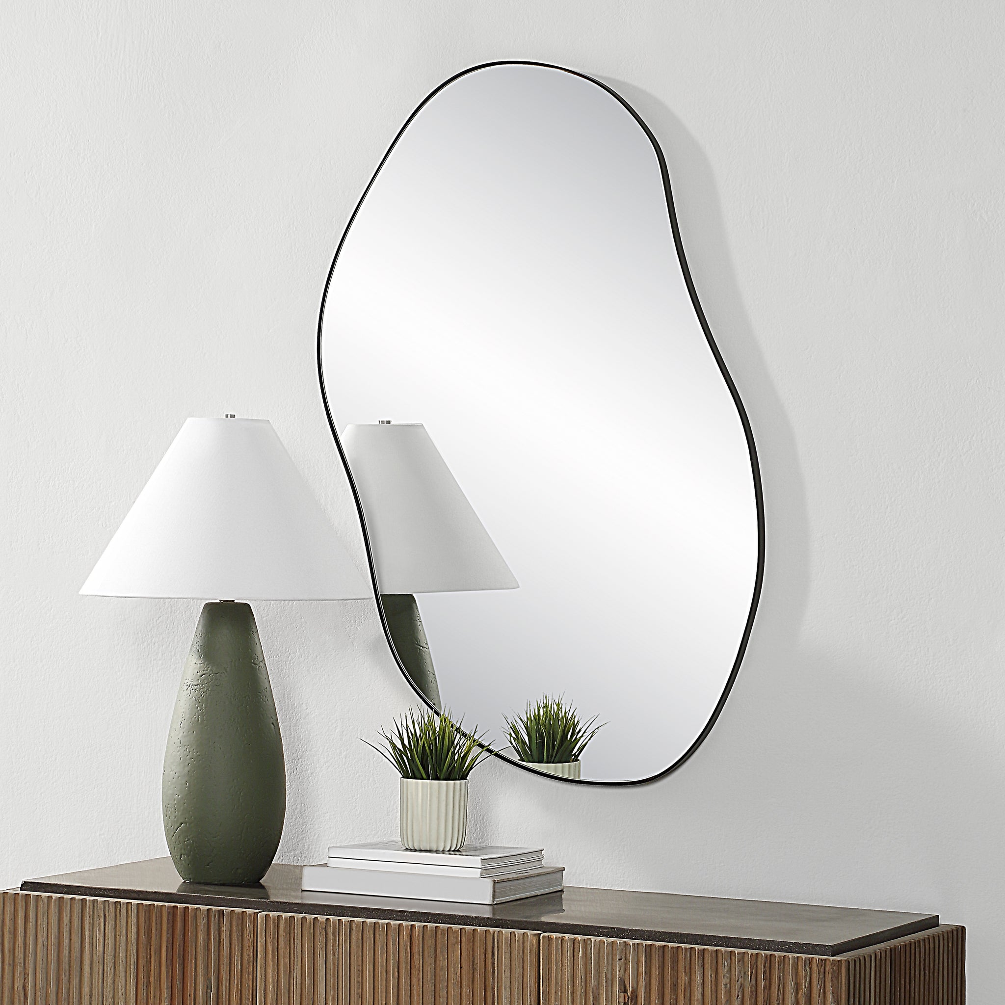 Jane Wall Mirror mounted on a wall above a wooden console, with a lamp and plant beside it.