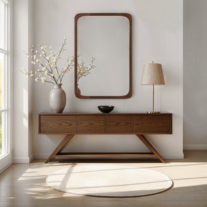 Sisley mirror displayed above a wooden console table with decorative vase and lamp in a bright room.
