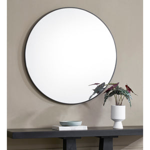 Posadas Wall Mirror with a round shape and black frame, displayed above a console table with decor.