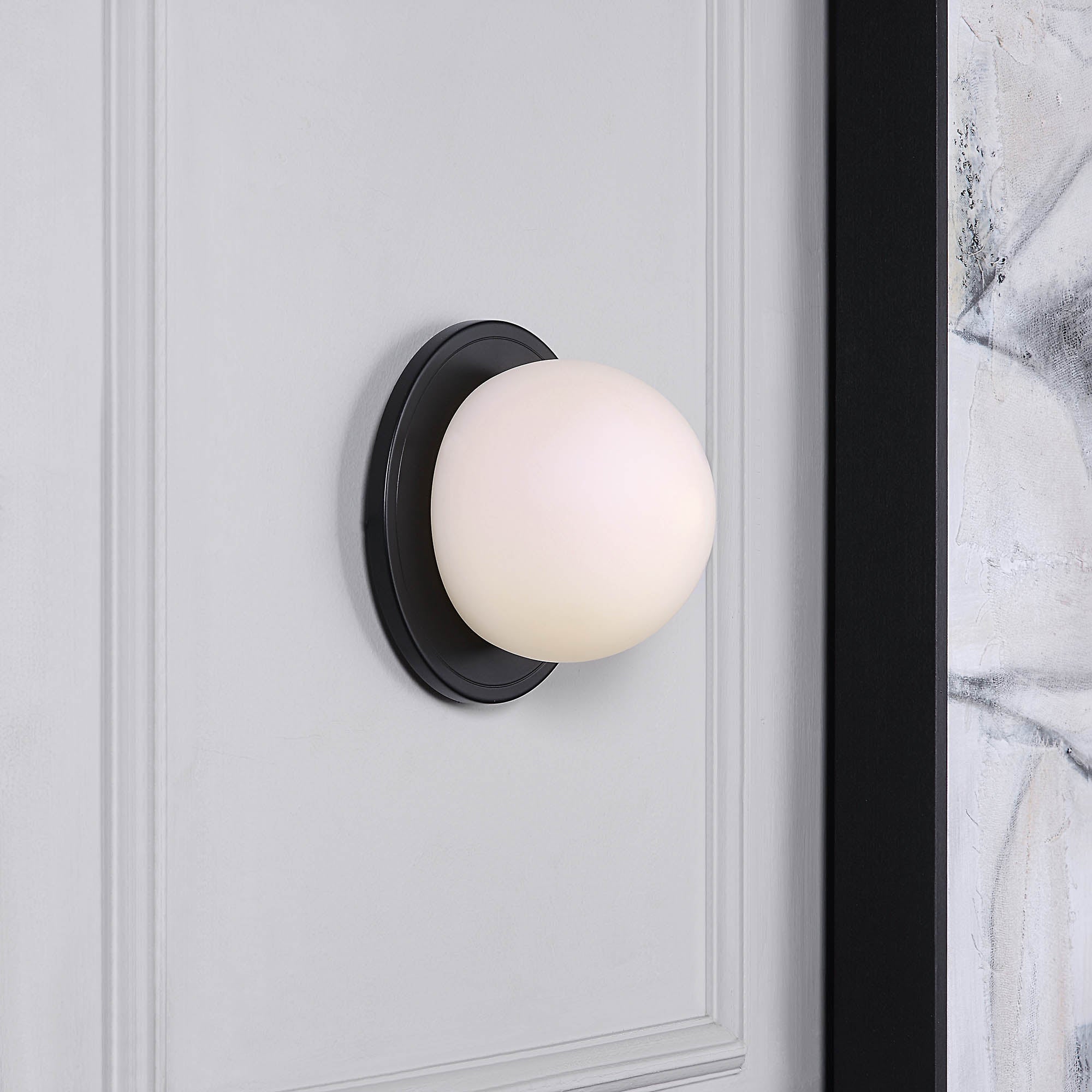 Sybil Wall Sconce installed on a gray wall, showcasing a white glass shade and black base