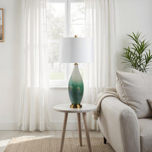 Wave table lamp placed on a side table in a living room, showcasing its green glass base and white shade