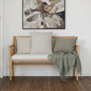 Pisces pillow on a bench with a green throw and artwork above.