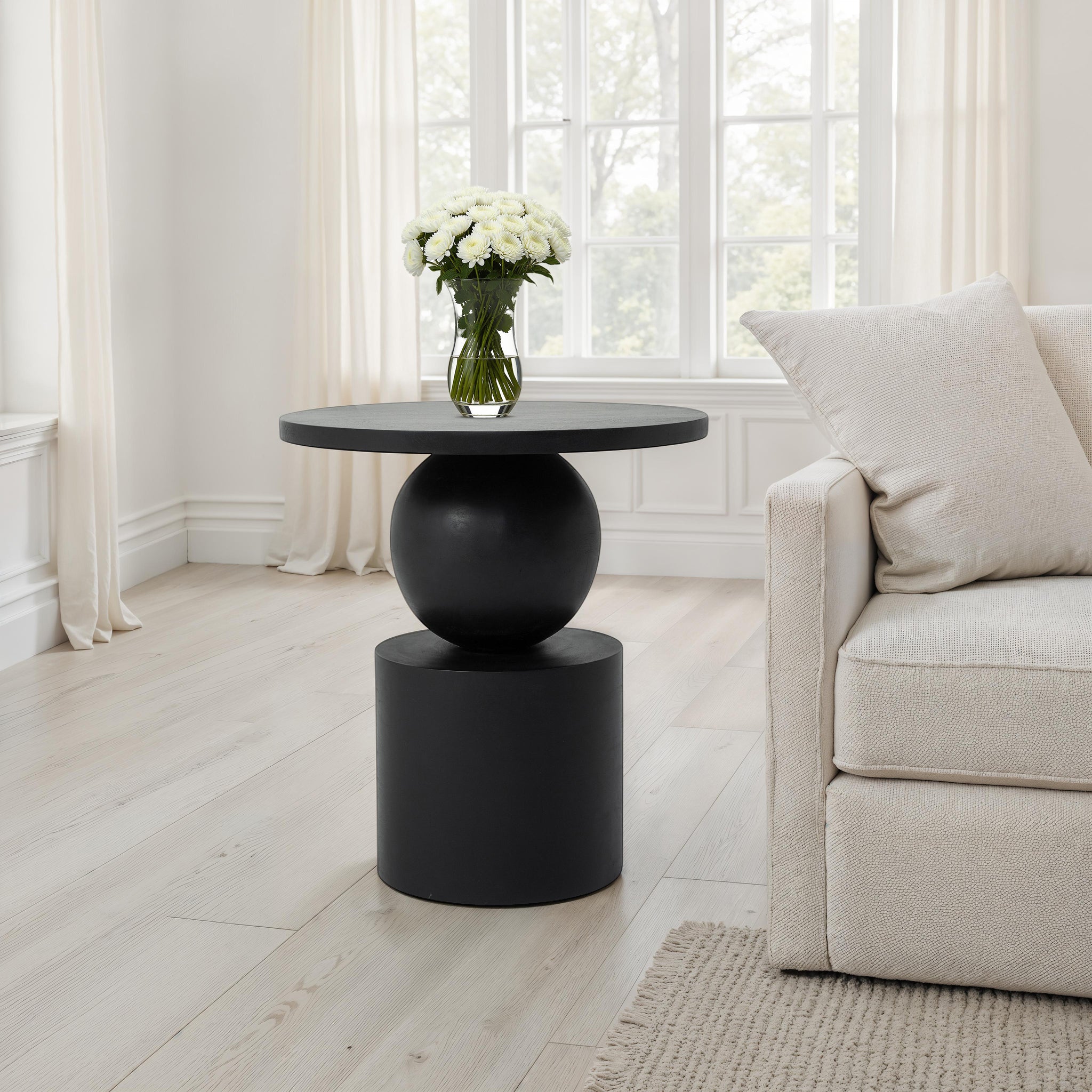Paola side table in a bright room next to a sofa, featuring a vase of flowers.