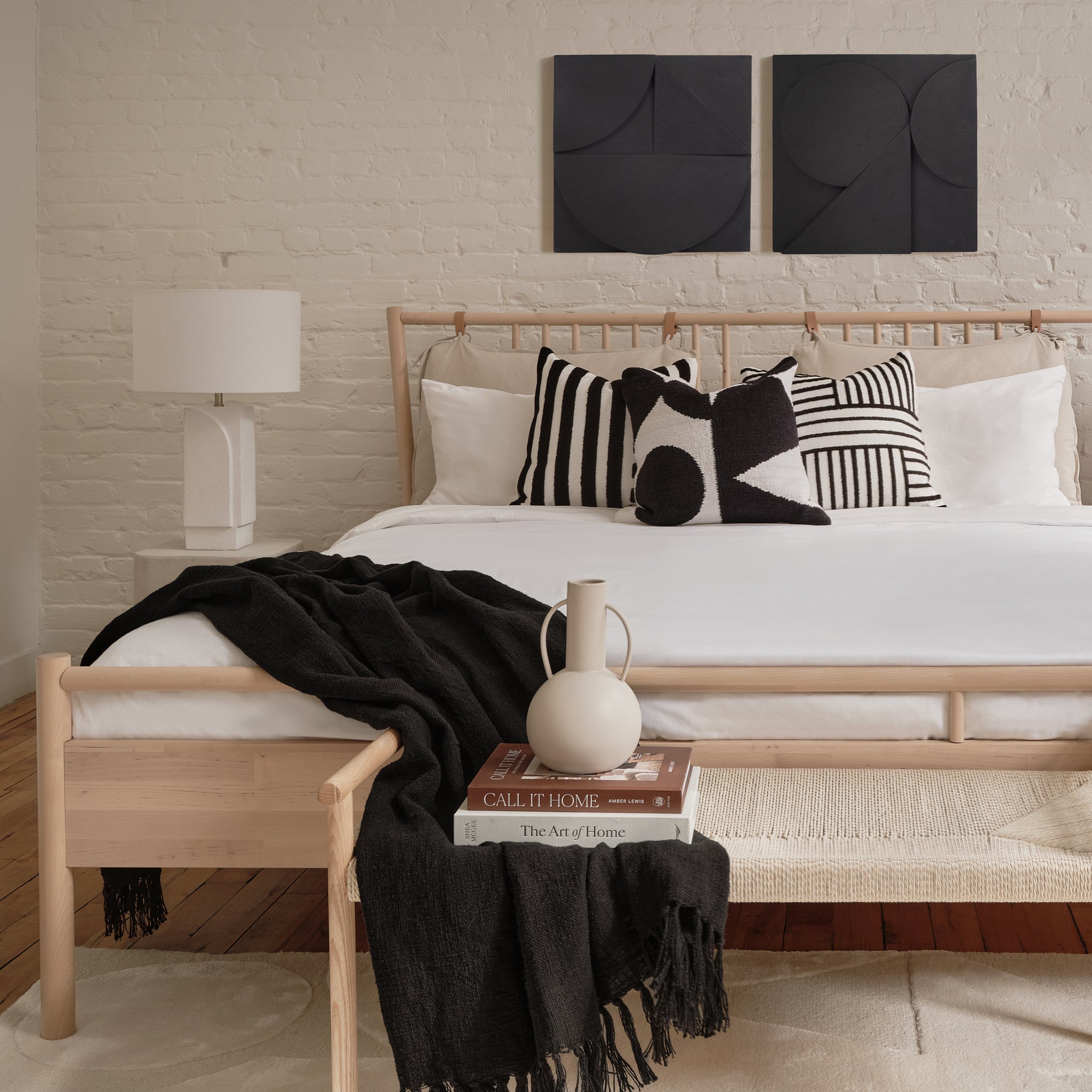 Mura wall decor displayed above a bed with black and white pillows in a cozy bedroom setting.