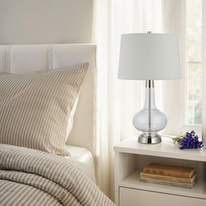 Lya Table Lamp on a nightstand beside a bed with striped bedding and a vase of flowers.