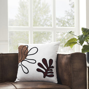 Erin Indoor Pillow placed on a brown leather couch with a window view