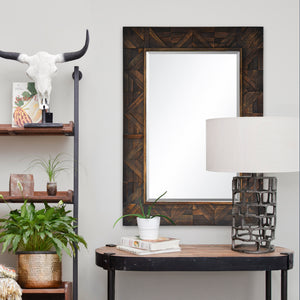 Madden Wall Mirror displayed in a room setting with plants, a lamp, and decorative items around it.