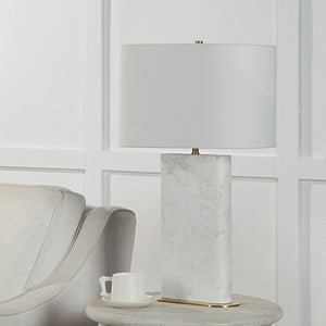 Irisa Table Lamp on a side table next to a gray armchair, featuring a white shade and marble base.
