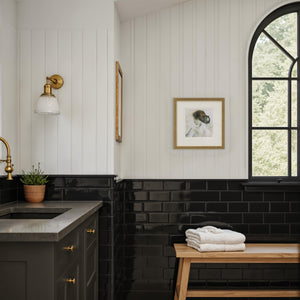 Penelope printed art displayed in a modern bathroom with black tiles and a gold light fixture