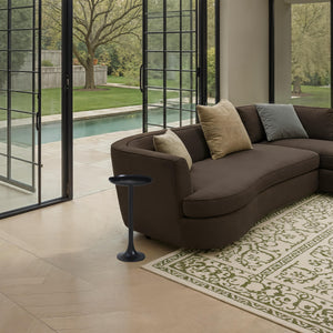 Fiora side table in a modern living room setting next to a curved brown sofa.