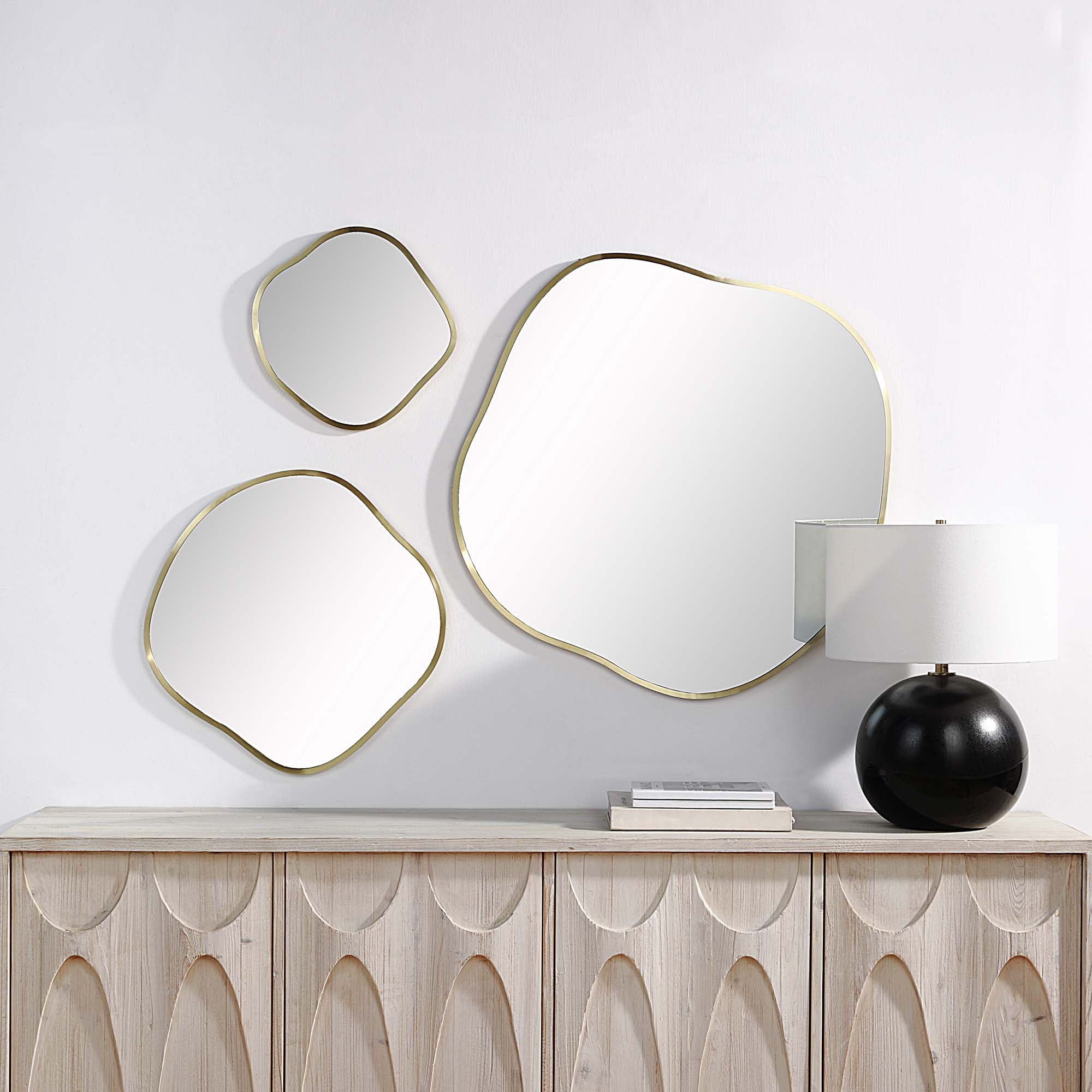 Nucleus Wall Mirrors arranged on a wall above a wooden sideboard with a lamp.