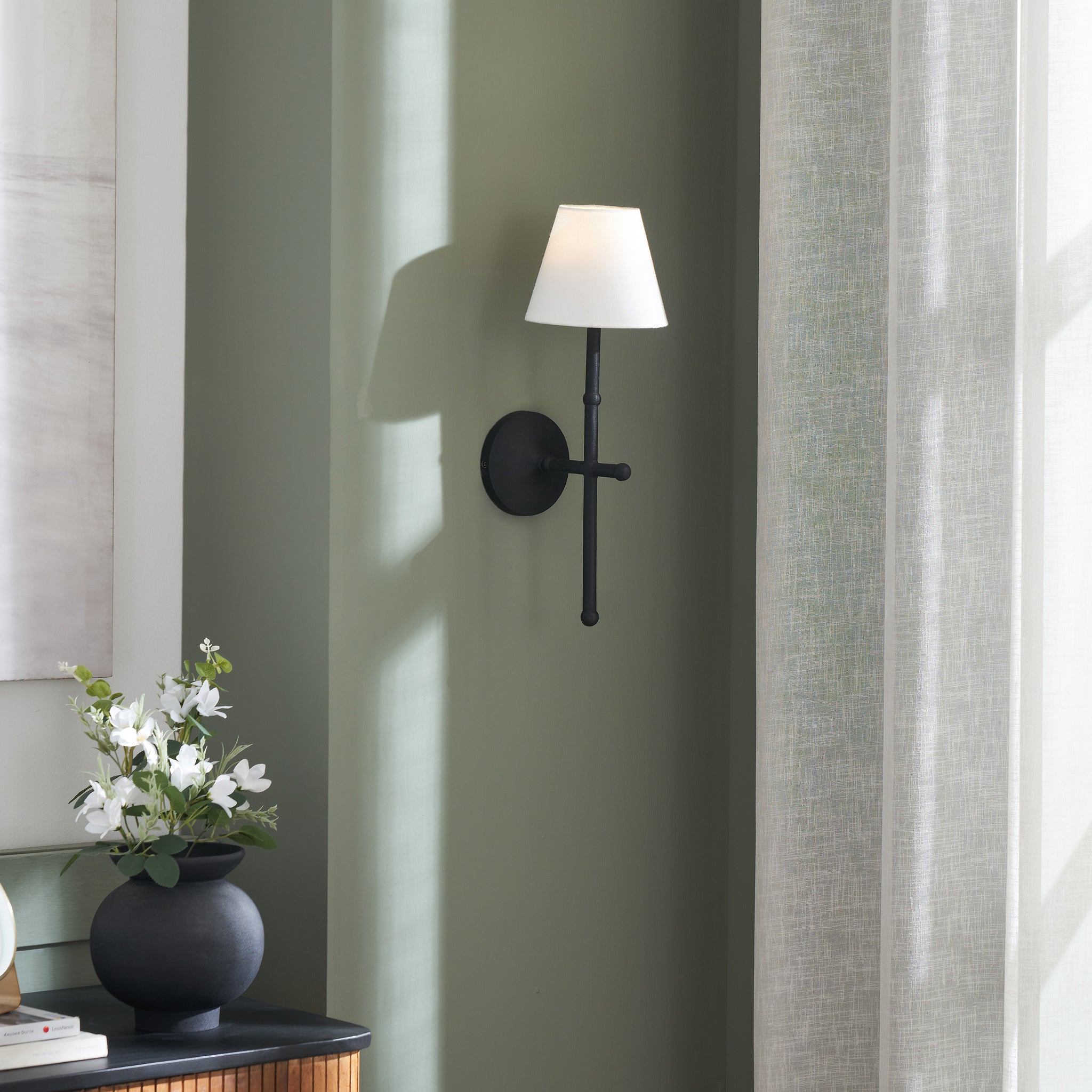 Kurosu wall sconce mounted on a green wall, with a decorative vase nearby