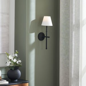 Kurosu wall sconce mounted on a green wall, with a decorative vase nearby