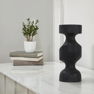 Severn by Renwil black wooden candle holder displayed on a marble table with books and a plant.