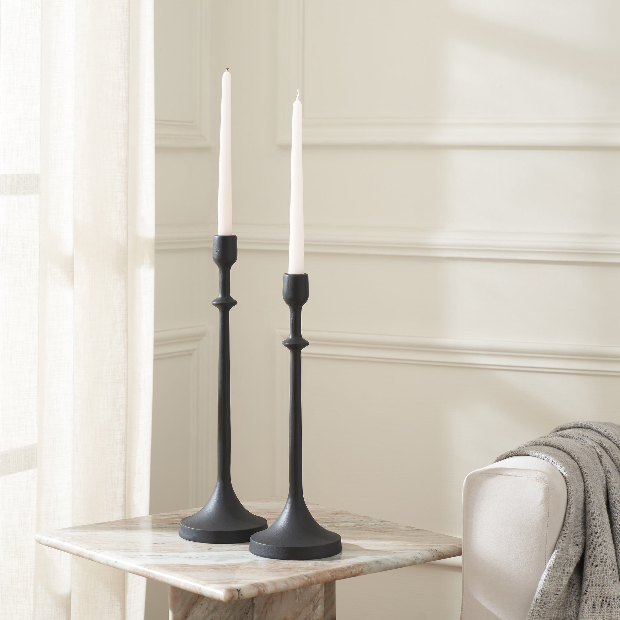 Albero Candle Holders in black with white candles, placed on a marble table in a bright room.