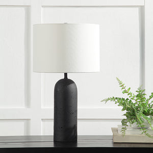 Augusta Table Lamp on a table with a white shade and black base, beside a plant