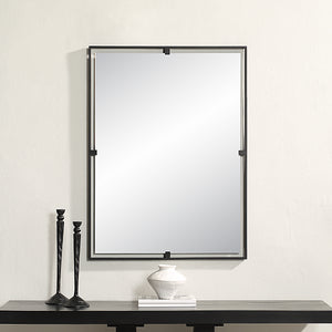 Marco Wall Mirror with a sleek black metal frame, reflecting light, mounted above a dark wood table with decorative items.