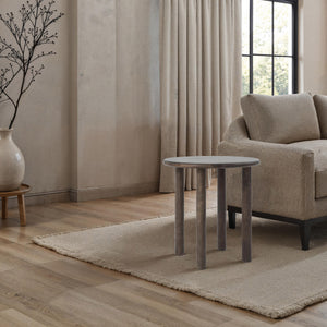 Cetus accent table placed in a living room setting beside a beige sofa and decorative vase.