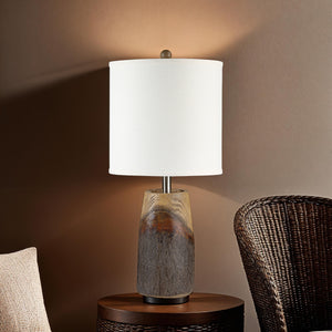 Vinca Table Lamp on a side table with a brown wall backdrop and a woven chair