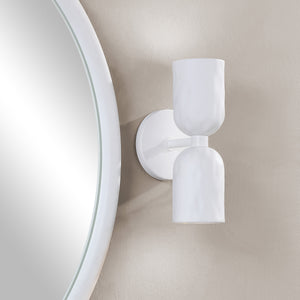 Akira Wall Sconce in white mounted beside a round mirror on a textured wall