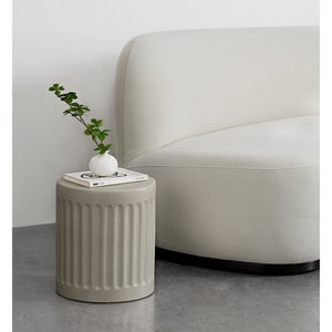 Lucian Table styled beside a curved sofa, holding a small vase and books.