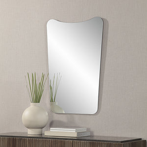 Selene Wall Mirror mounted on a textured wall, beside a vase and stacked books.