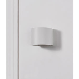 Zak Wall Sconce mounted on a white wall, featuring a simple cylindrical design.