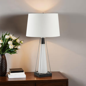 Navagio Table Lamp placed on a wooden table with a vase of flowers, featuring a white shade and modern design.