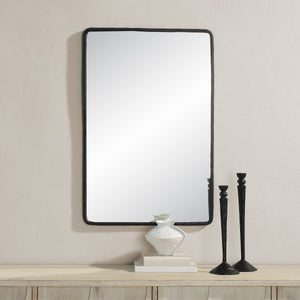 Jorah Wall Mirror with a black frame, rectangular shape, mounted on a light wall, alongside decorative items on a wooden table.