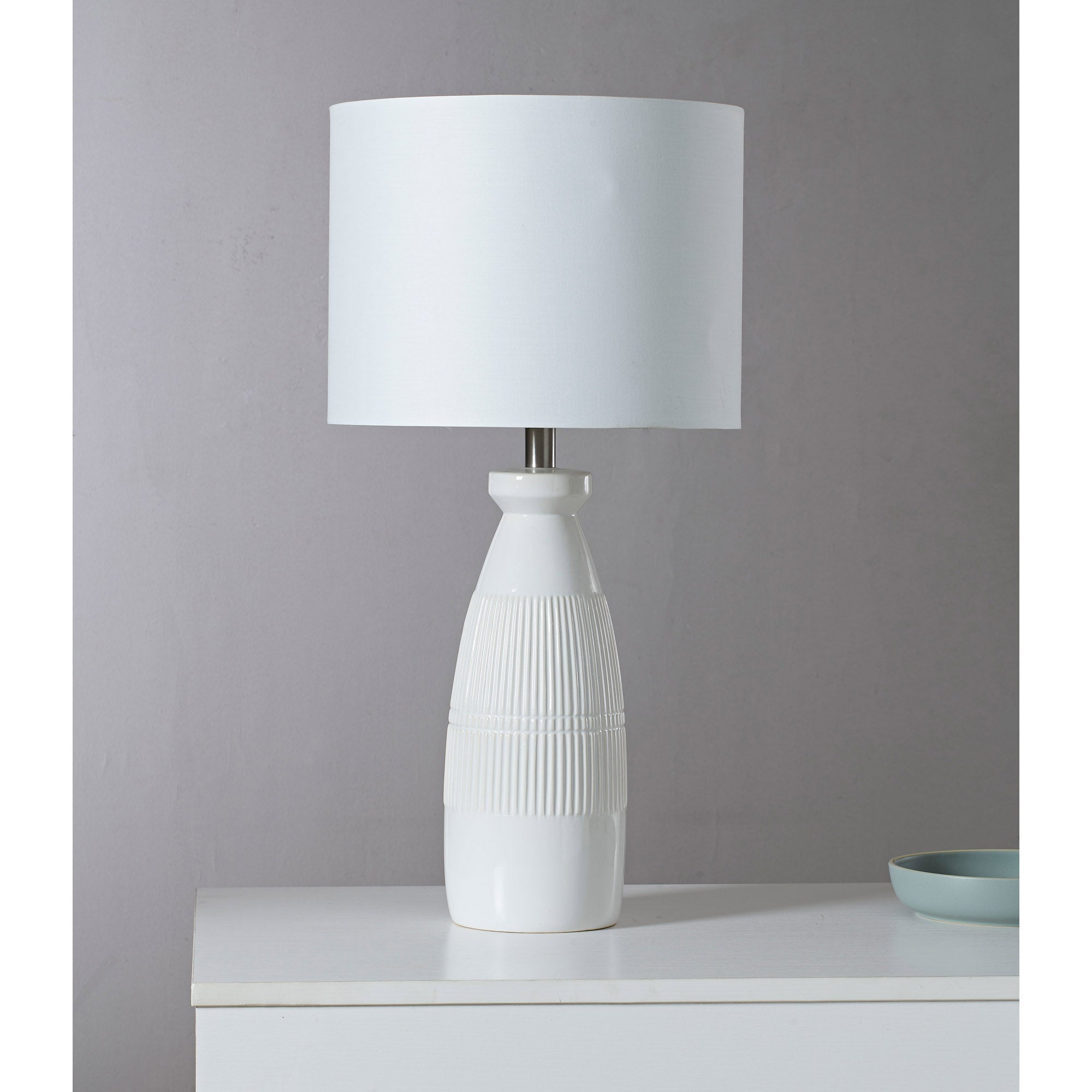 Nado Table Lamp on a white surface with a light gray background, featuring a white shade and ribbed base