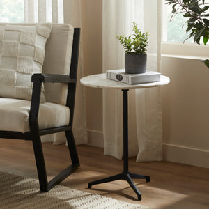Barker Side Table styled in a living room with a plant and books, next to a modern armchair.