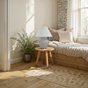 Iulia Table Lamp on a wooden side table next to a bed with decorative pillows