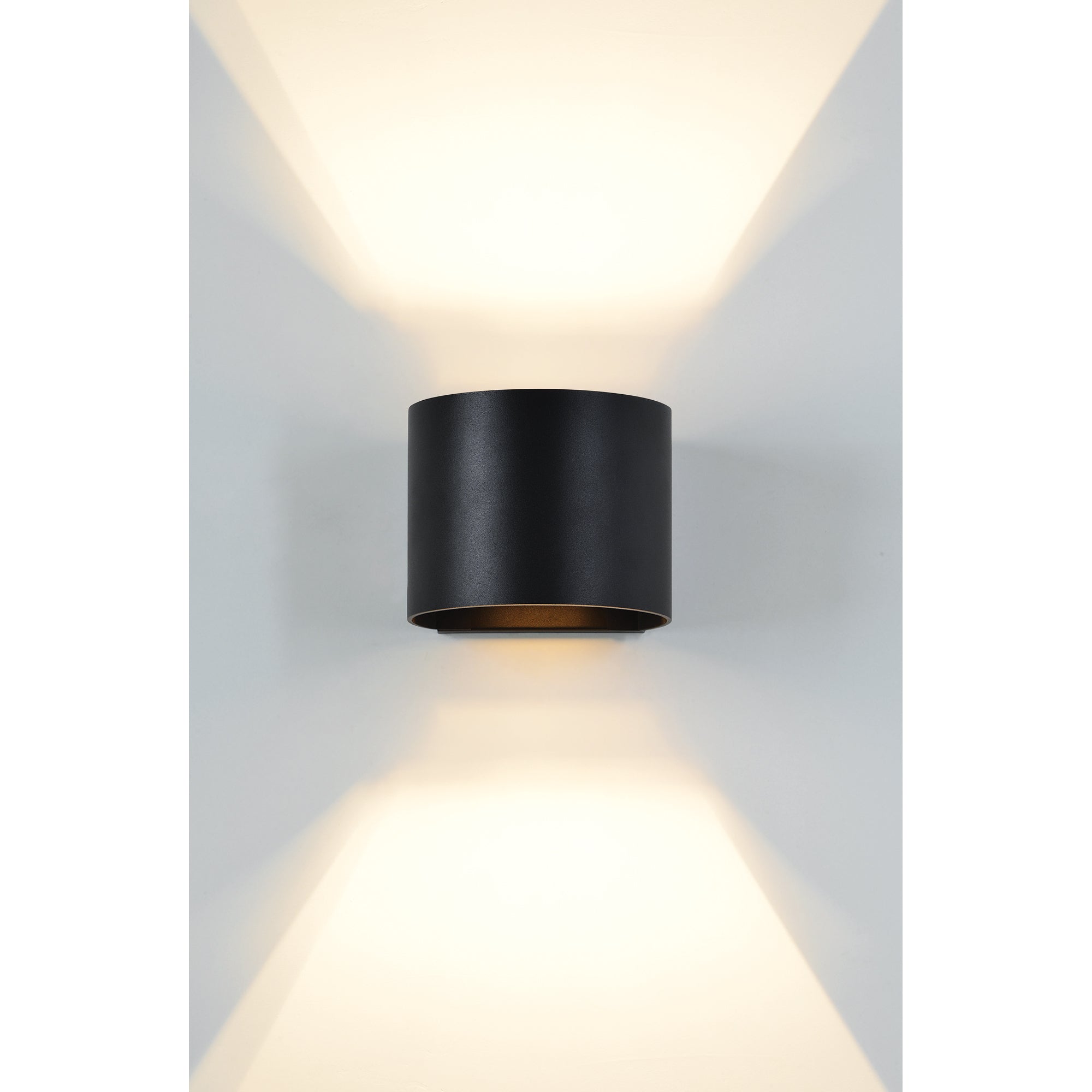 Lark Wall Sconce in matte black, illuminating a wall with upward and downward light.