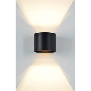 Lark Wall Sconce in matte black, illuminating a wall with upward and downward light.