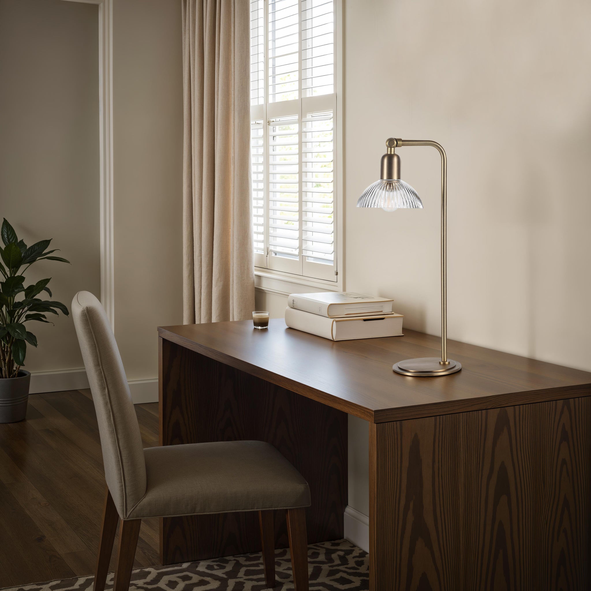Samos table lamp on a modern desk with books and a plant, bright room ambiance.