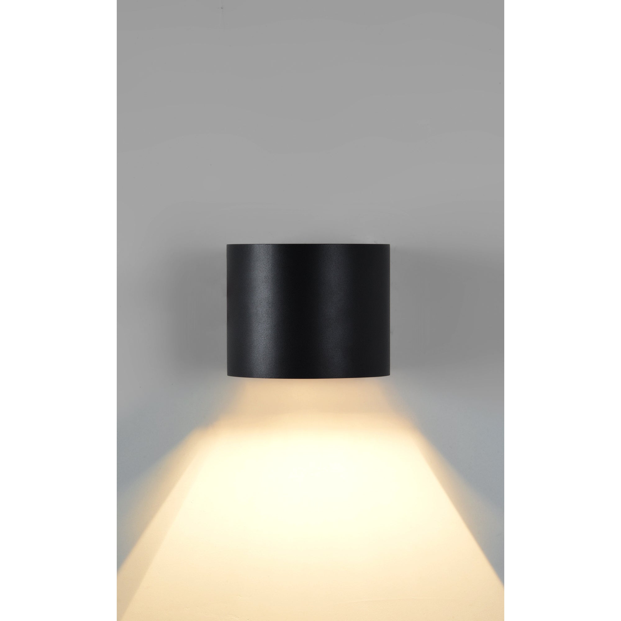 Lark Wall Sconce in matte black, casting light downwards with a sleek cylindrical shape.