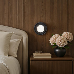 Haloa wall sconce mounted beside a bed with a wooden wall, flowers, and decor
