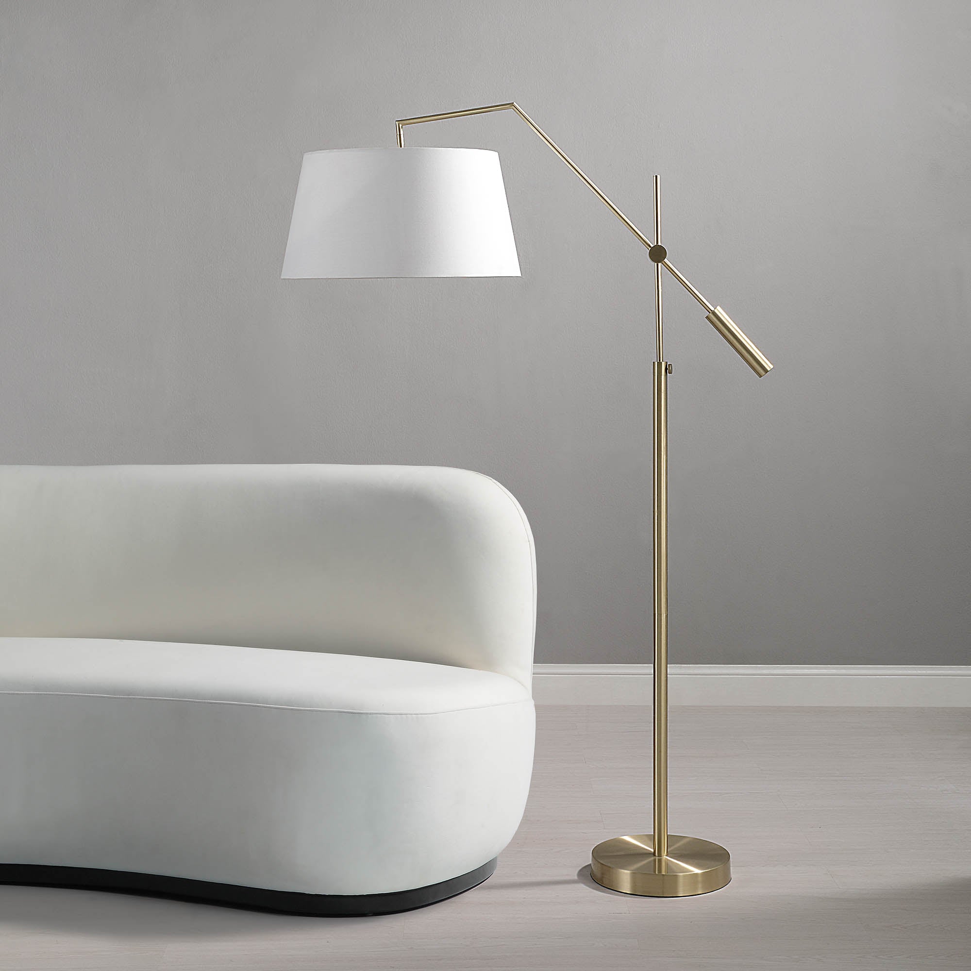 Claire Floor Lamp in brass positioned next to a white curved sofa against a gray wall.