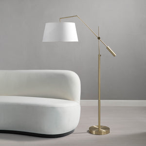 Claire Floor Lamp in brass positioned next to a white curved sofa against a gray wall.