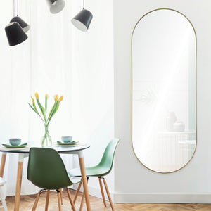 Marius Full Length Mirror in an oval shape with a gold frame, displayed in a bright dining area with green chairs.