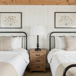 Zyra Table Lamp on a nightstand between two beds, cozy bedroom setting with artwork.
