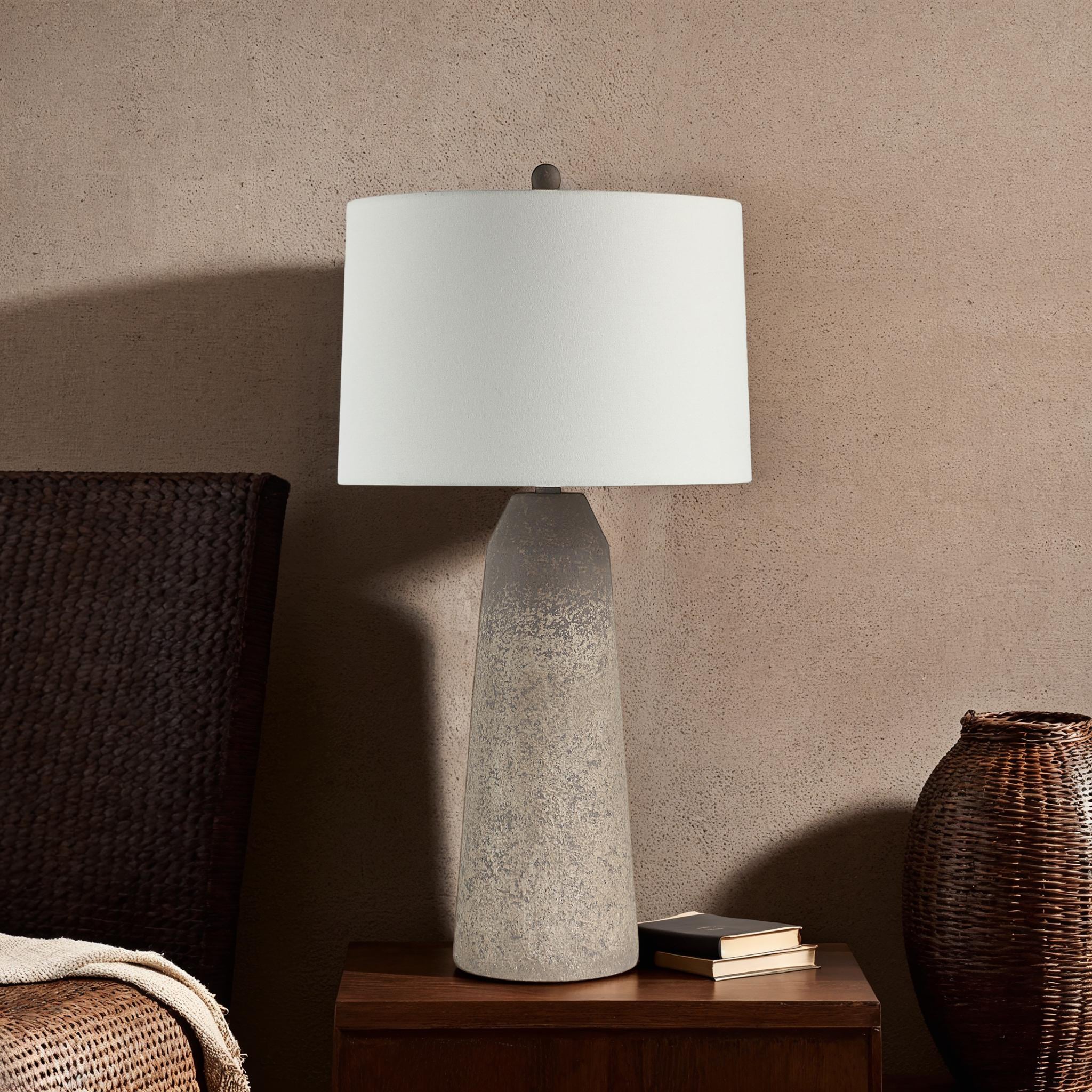 Limon Table Lamp by Renwil on a nightstand against a textured wall, with a white shade.