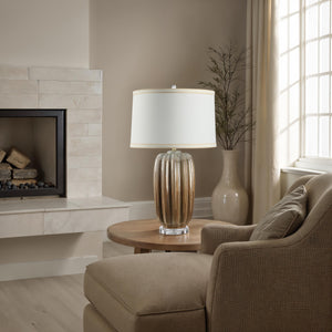 Lumeo table lamp on a round wooden table next to a cozy armchair in a living room.