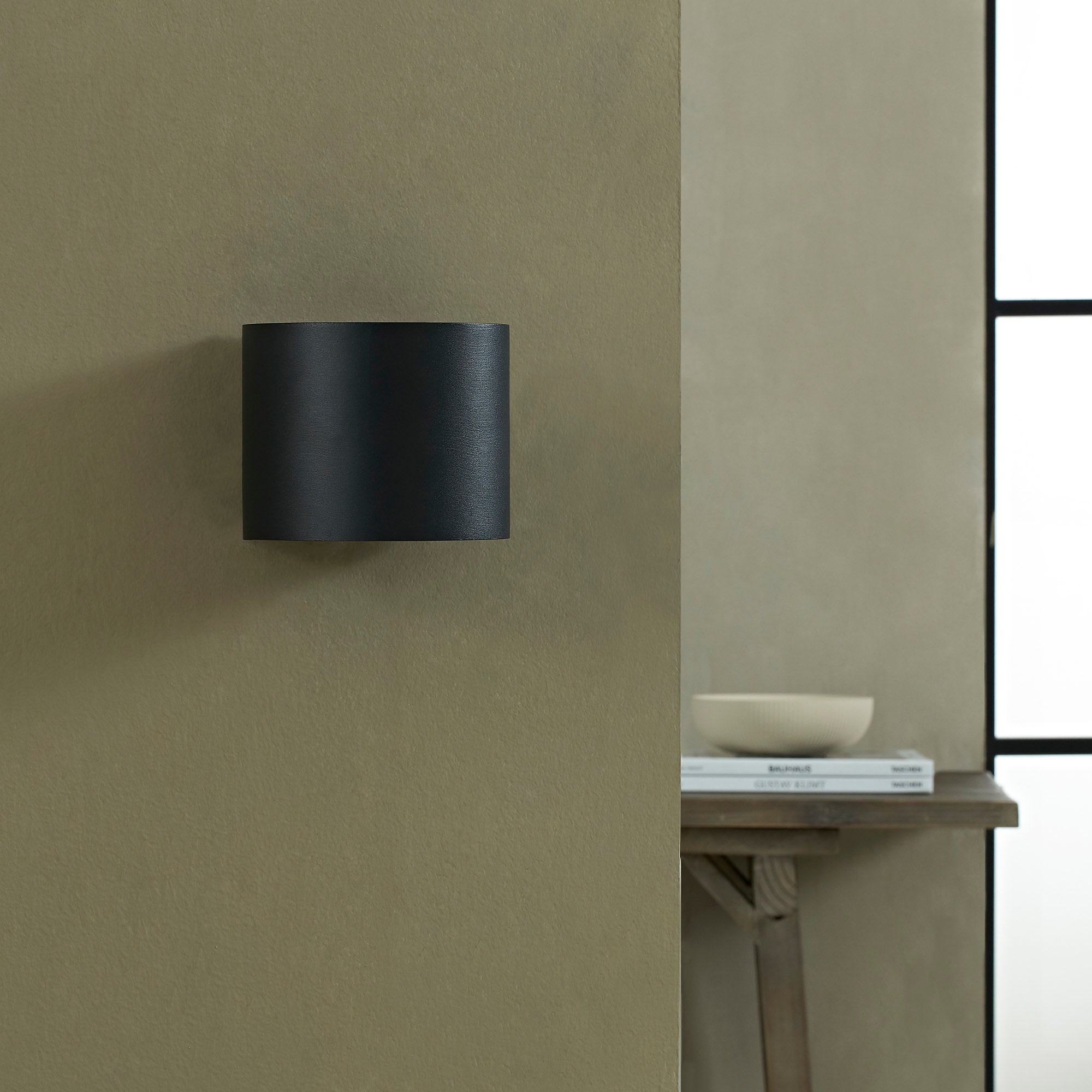 Lark Wall Sconce in matte black installed on a textured wall, complementing a minimalist decor.