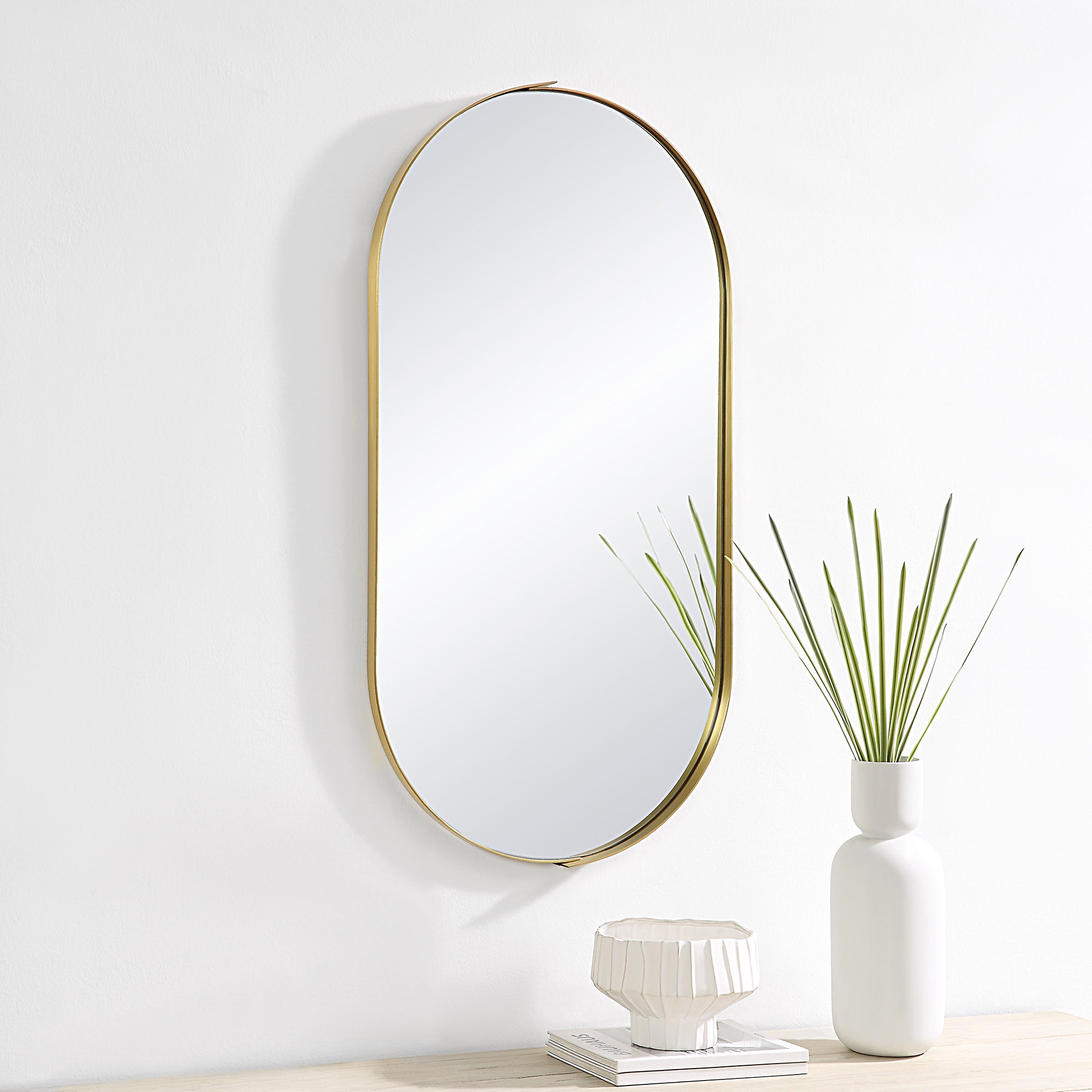 Aleah Wall Mirror mounted on a wall beside a white vase and decorative items.
