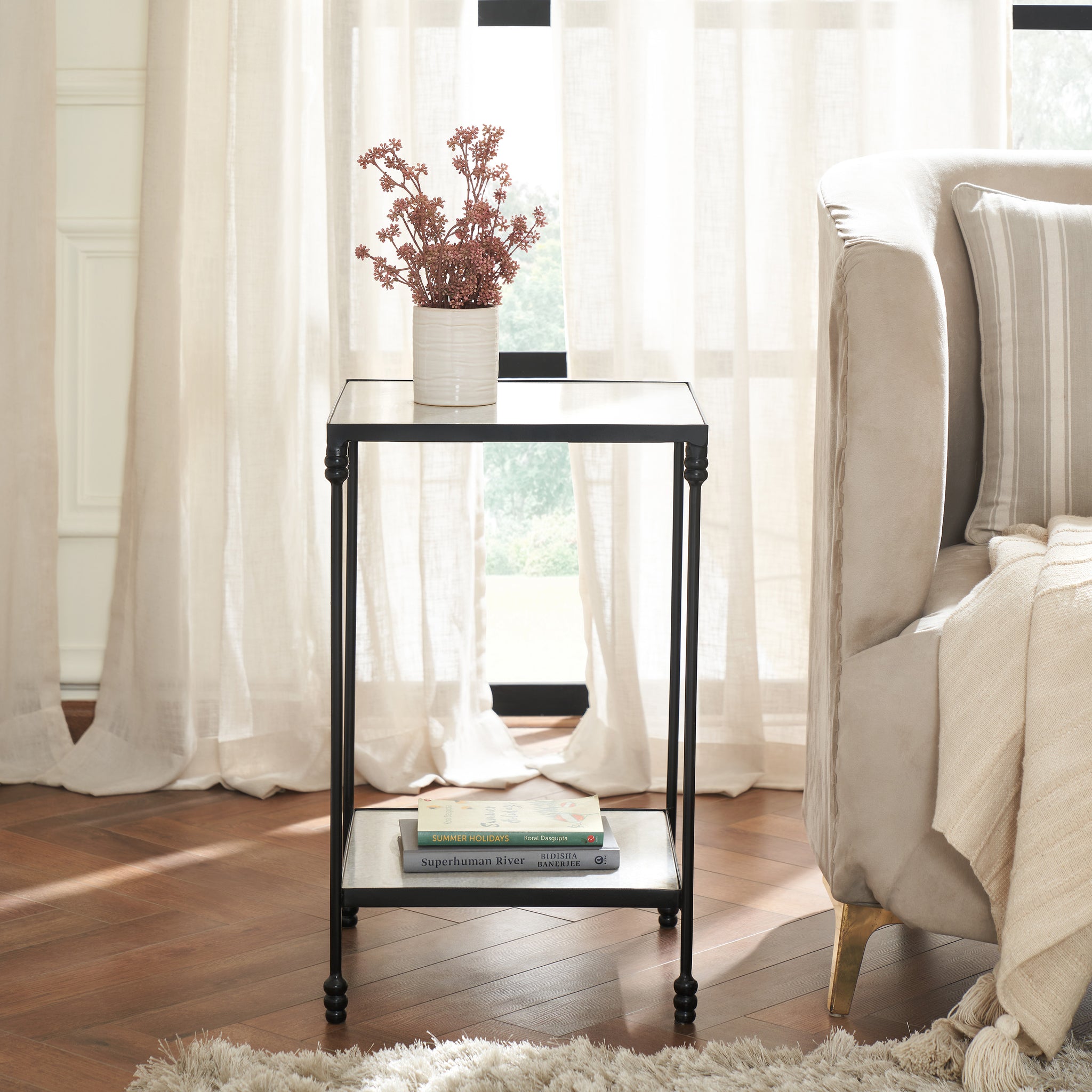 Giulia table styled with a vase and books, placed beside a sofa in a bright room.
