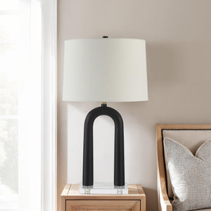 Pisa Table Lamp placed on a nightstand beside a beige sofa, featuring a black base and white shade.